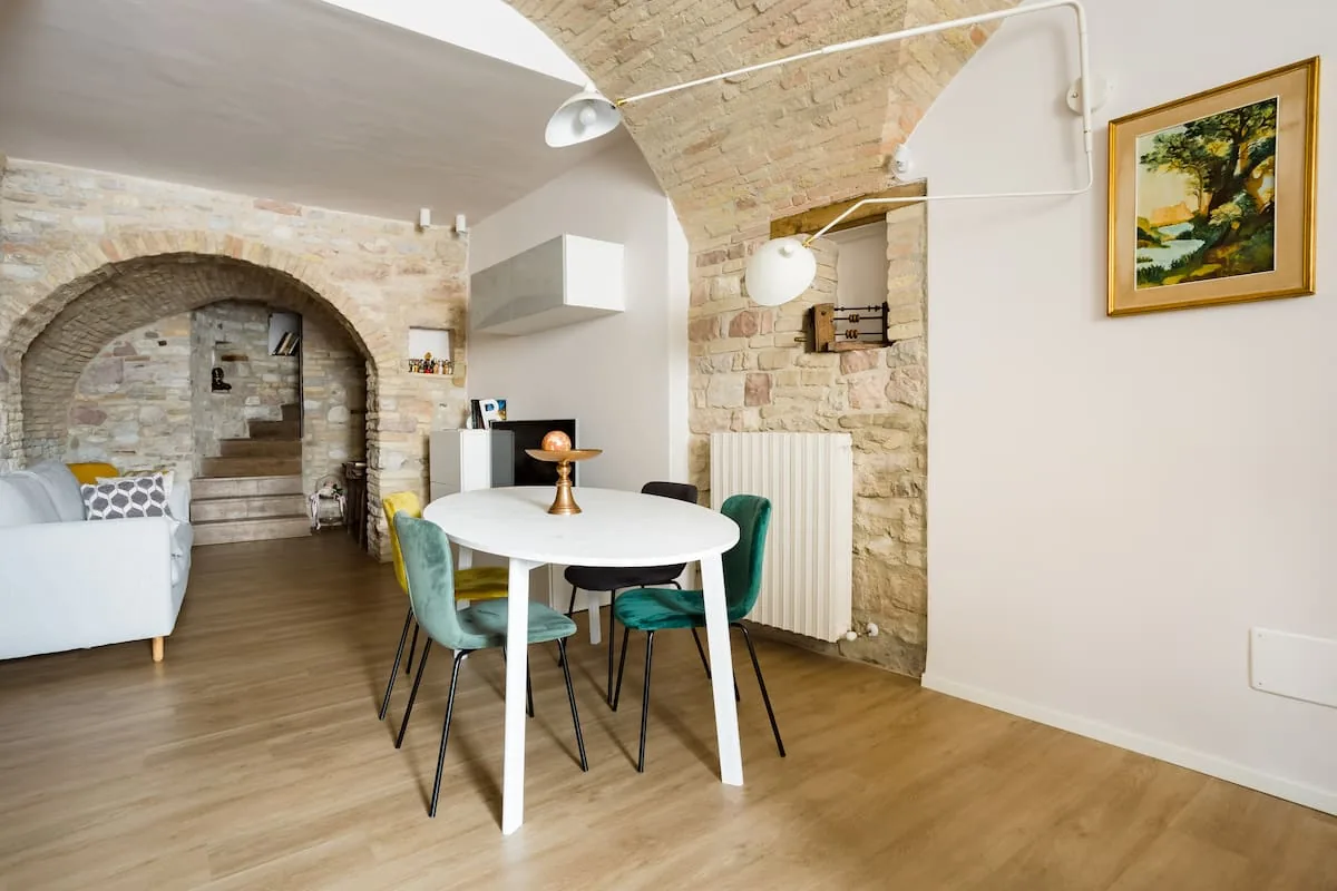 Zona pranzo con tavolo bianco e divano letto sotto l'arco in pietra